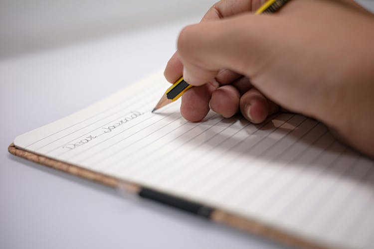 A Person Writing On A Journal 