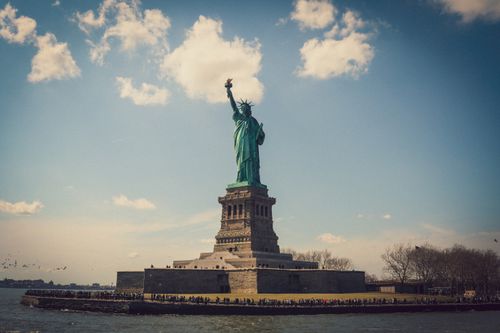 Free Scenic view of the Statue of Liberty with a clear blue sky and scattered clouds. Stock Photo