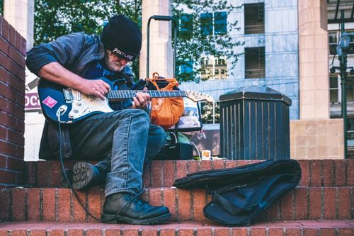Free A street musician playing an electric guitar on urban brick steps, creating a vibrant city vibe. Stock Photo