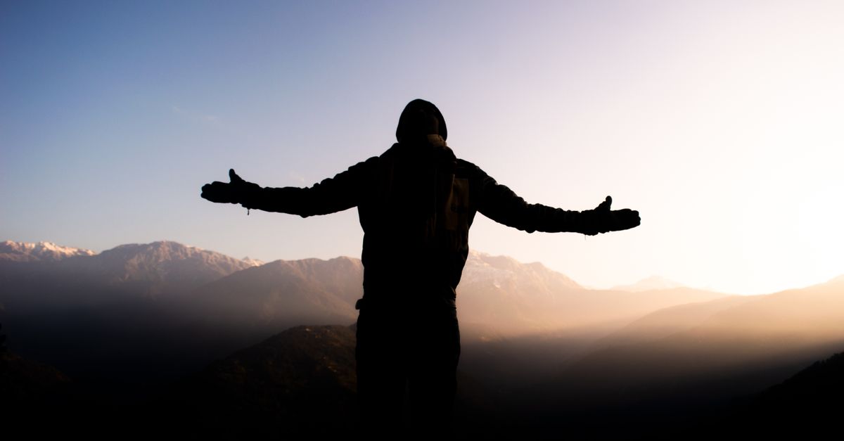 person standing on a balcony at sunrise, arms stretched, looking at the sky