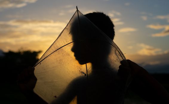 A young boy's silhouette emerges against a vibrant sunset while holding a kite, creating a serene scene.