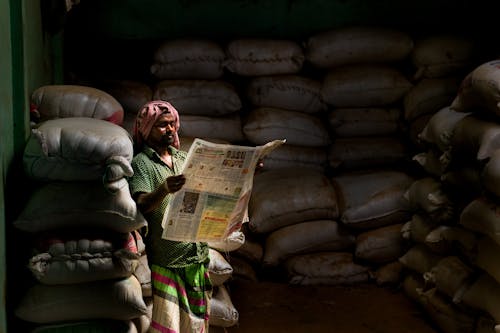 Free Man Reading Newspaper inside a Storeroom with Stack of Sacks Stock Photo
