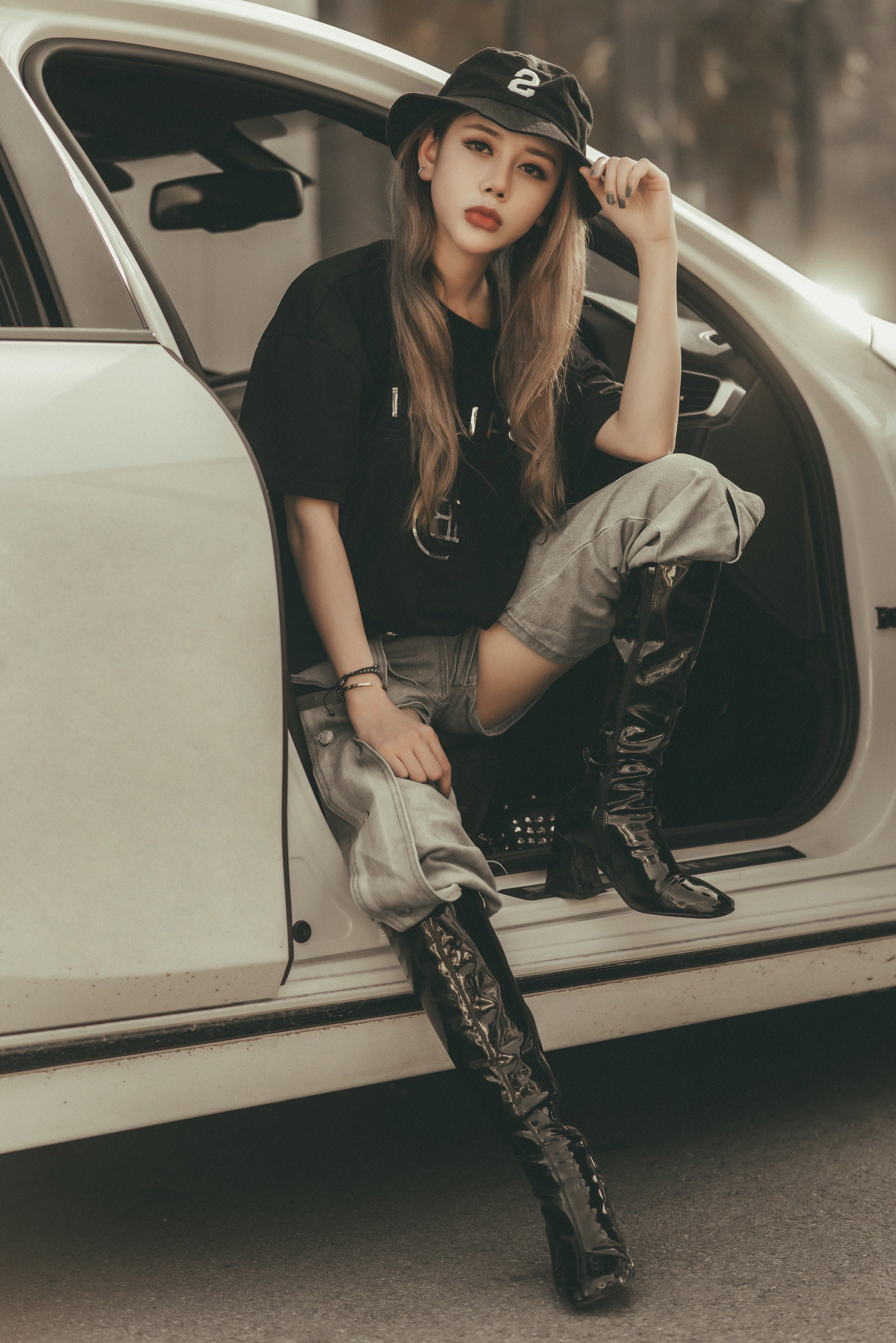 Stylish woman sitting in a car doorway wearing trendy streetwear and boots.
