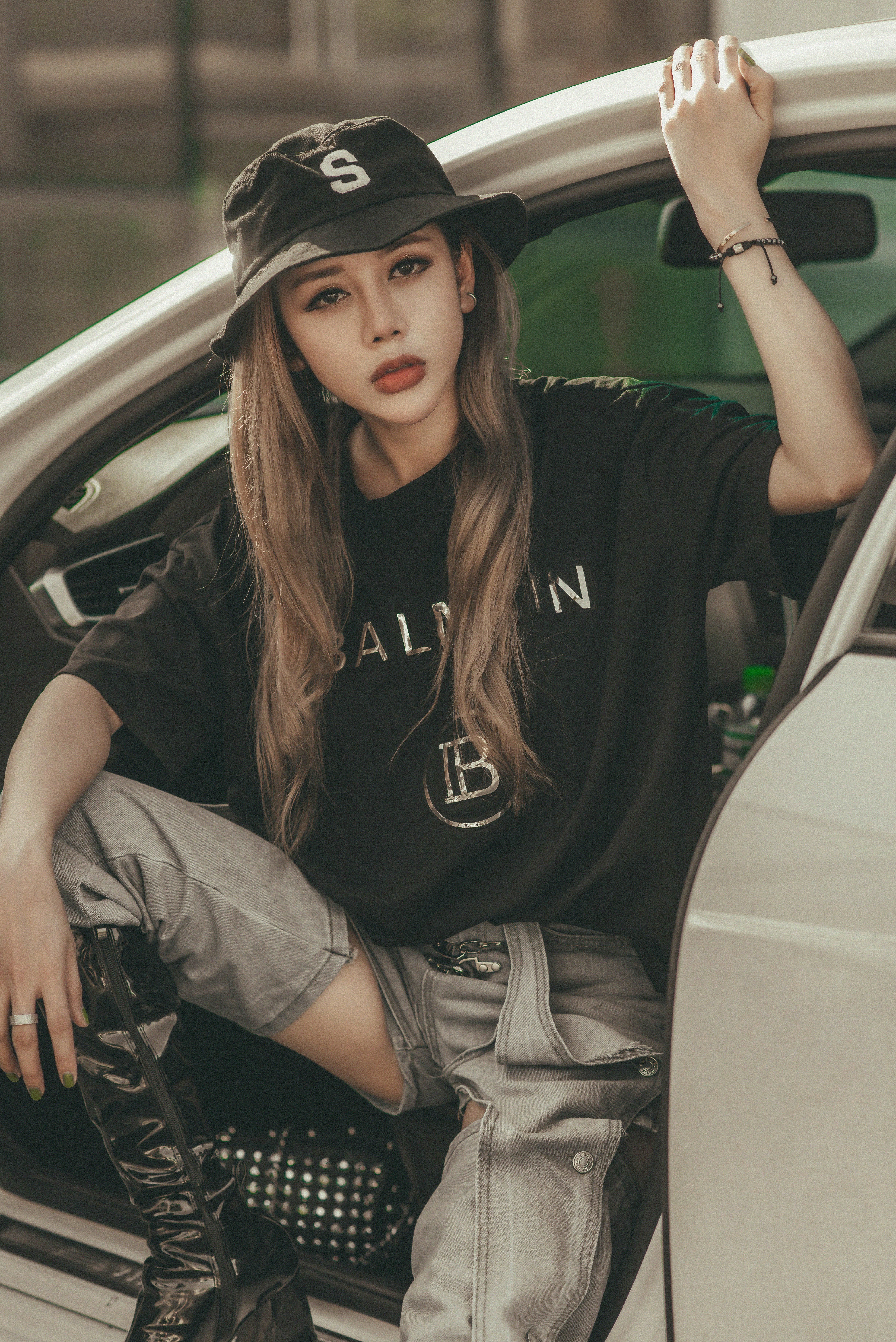 Stylish woman wearing a bucket hat and denim jeans poses confidently in a car.