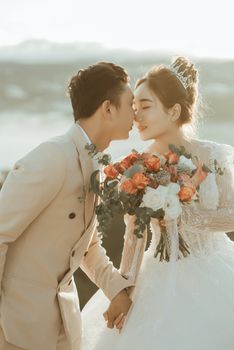 An Asian couple shares a tender moment on their wedding day, holding a vibrant flower bouquet.