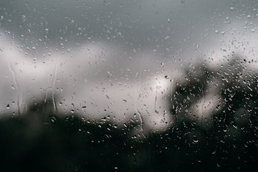 Artistic close-up of raindrops on a window with an out-of-focus cloudy background.