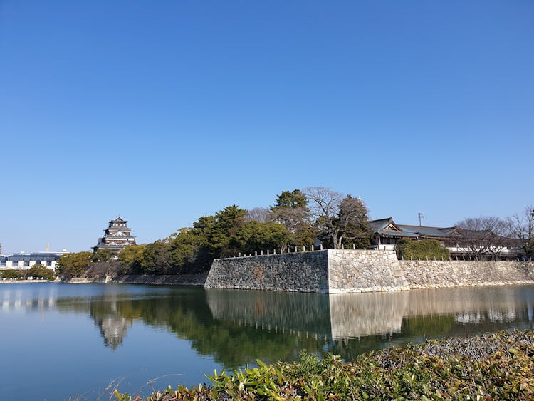 Gray Stone Wall Near Body Of Water With View Of Hiroshima Castle In Japan Under Blue Sky