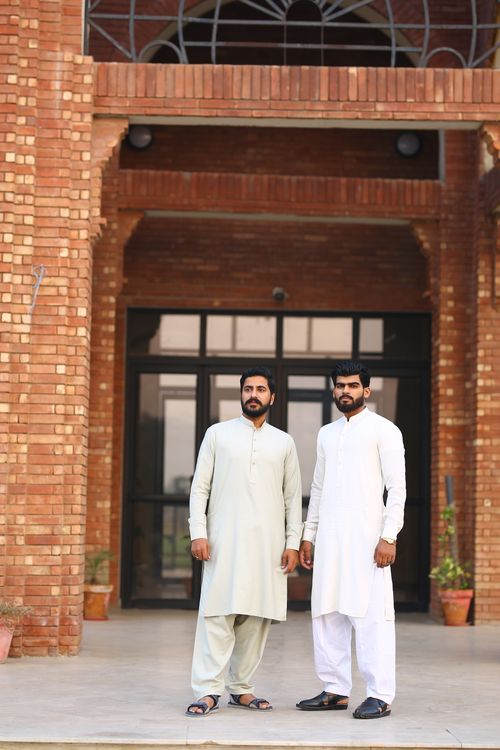 Free Two men in traditional Pakistani kurta standing outside a brick building. Stock Photo