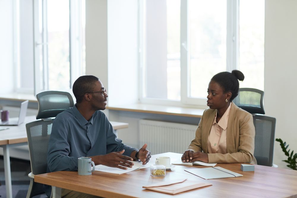 Two colleagues talking across a table with mugs and papers