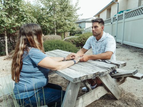 Free A couple holding hands while sitting at a rustic picnic table in an outdoor setting. Stock Photo