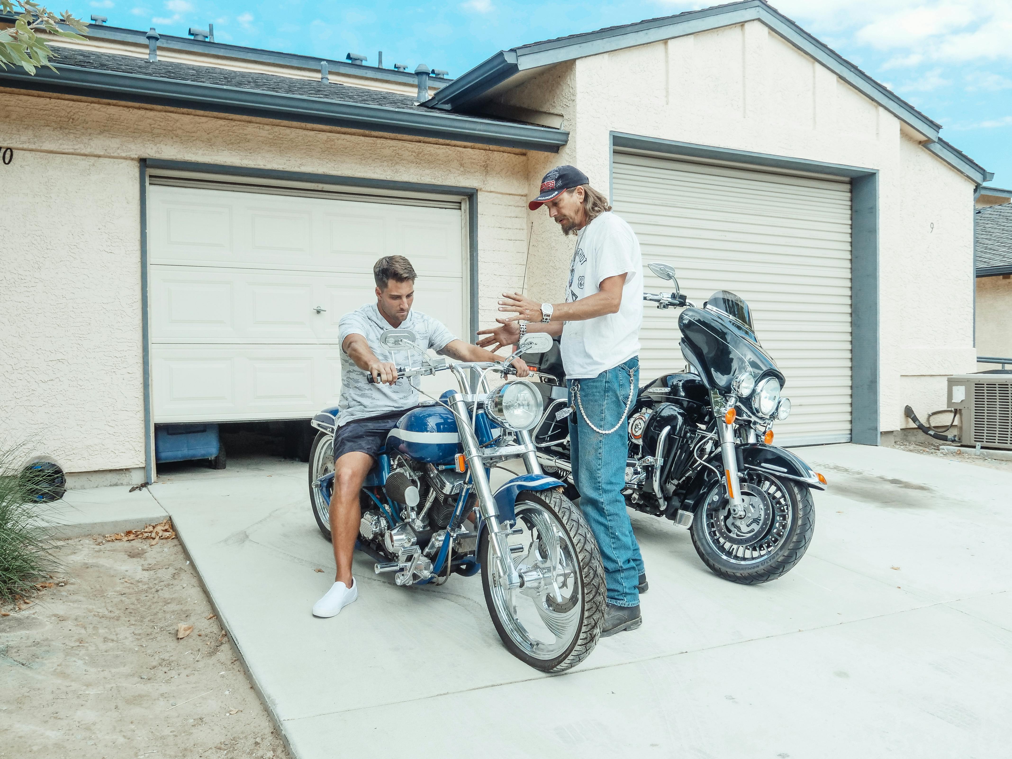 Two men enjoy quality time with motorcycles outside a garage, symbolizing parenthood and bonding.