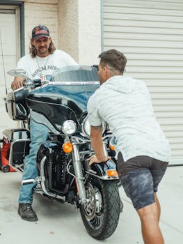 Two men conversing near a large motorcycle outdoors, showcasing casual style and urban life.