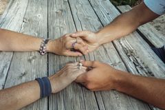 Two pairs of hands gently holding across a weathered wooden table, symbolizing connection and support.