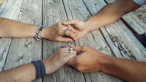 Two pairs of hands gently holding across a weathered wooden table, symbolizing connection and support.