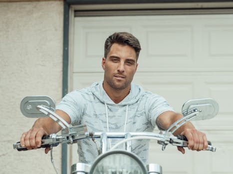 A confident man poses with a motorcycle outdoors, exuding style and adventure.