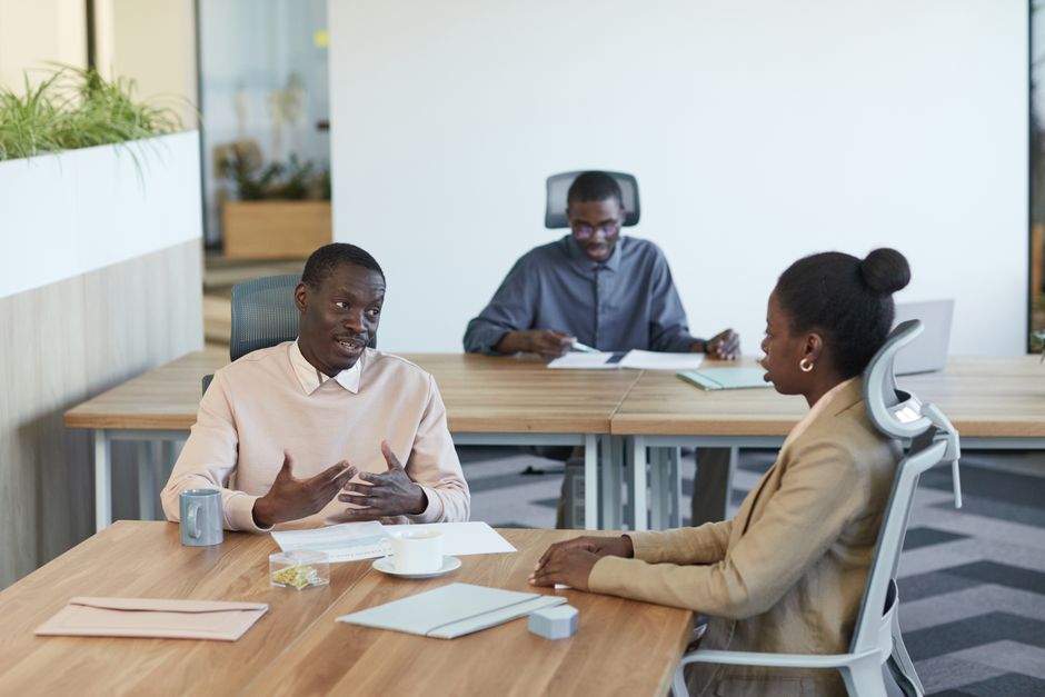 Três profissionais participando de uma reunião em um espaço de trabalho interno.