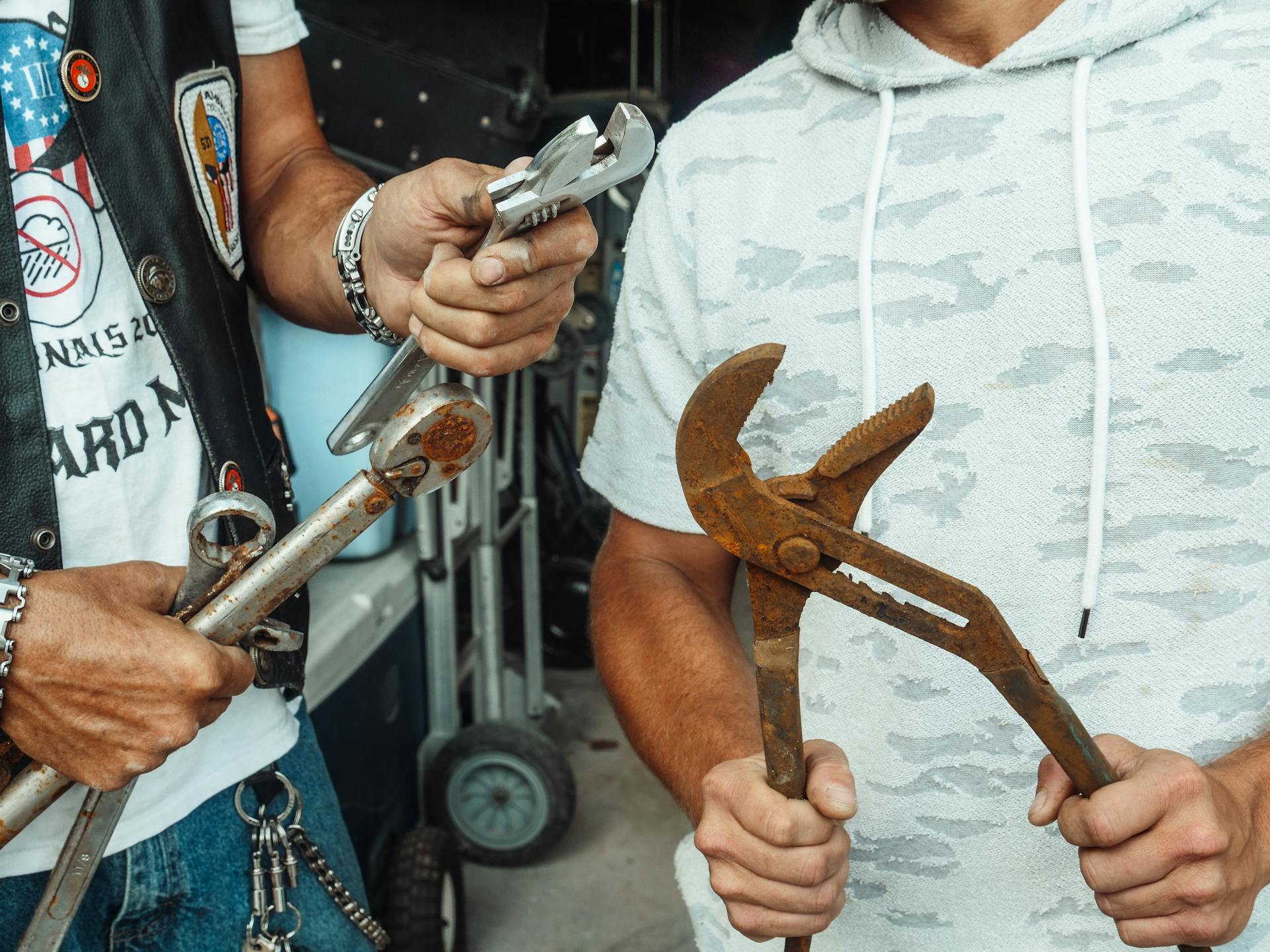 A father and son bonding in a garage while holding wrenches and pliers.