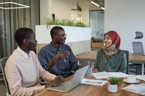 Free Three colleagues engaged in a collaborative discussion around a table in a modern office setting. Stock Photo