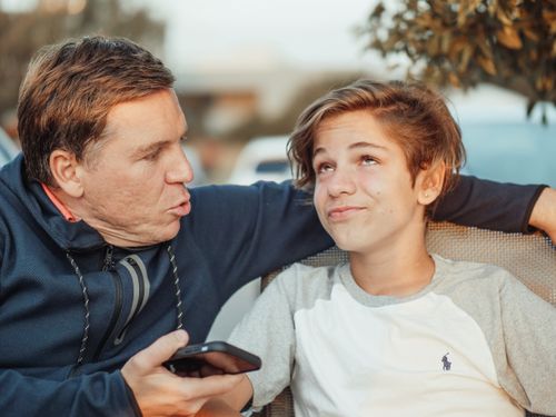 Free Playful interaction between father and son in a casual outdoor environment, captured in a candid moment. Stock Photo