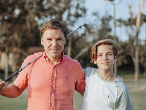 Free Boy in White Crew Neck Shirt Standing Beside Man in Red Button Up Shirt with a Golf Club Stock Photo