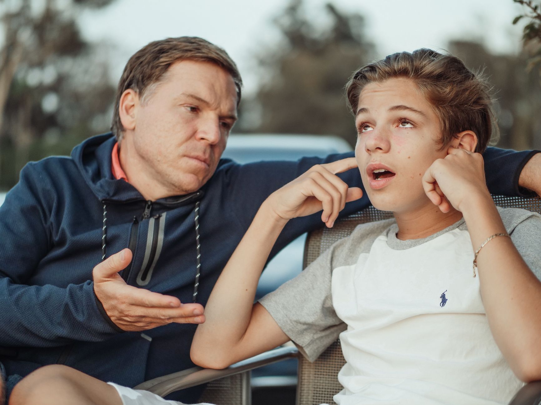 Father and teenage son sitting face to face during a hard conversation outdoors