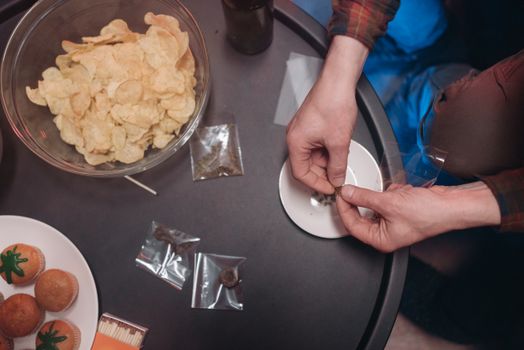Hands rolling a joint with snacks on a table, featuring chips and cupcakes.