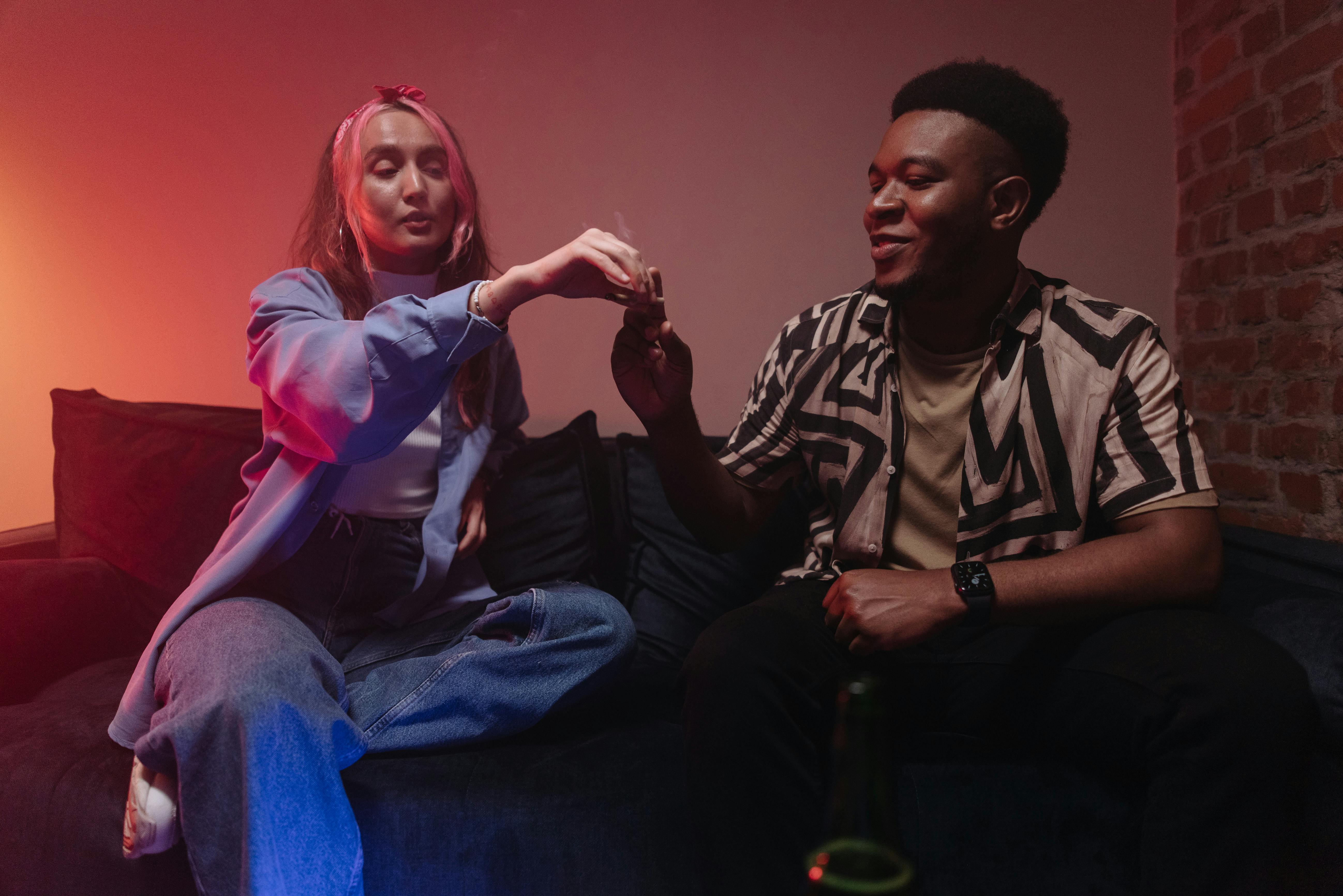 Two friends enjoying a relaxed evening indoors, sharing a joint and smiling.
