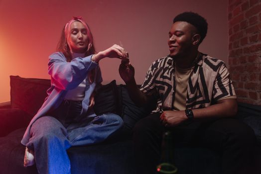 Two friends enjoying a relaxed evening indoors, sharing a joint and smiling.