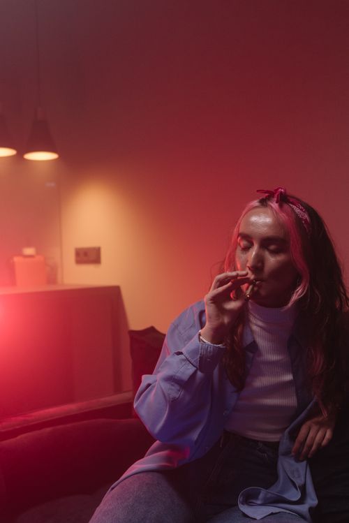 Free A young woman smokes indoors, surrounded by vibrant lighting. Stock Photo