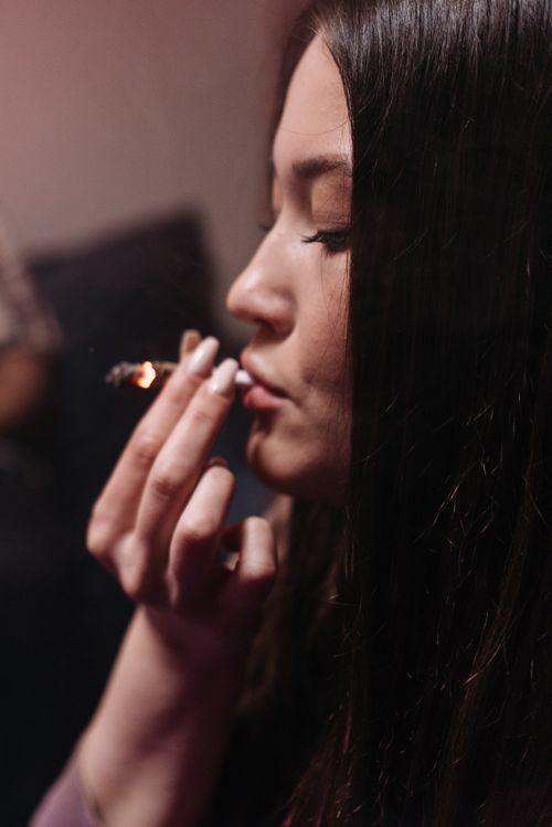 Free Profile of young woman smoking marijuana indoors, creating a moody ambience with soft lighting. Stock Photo