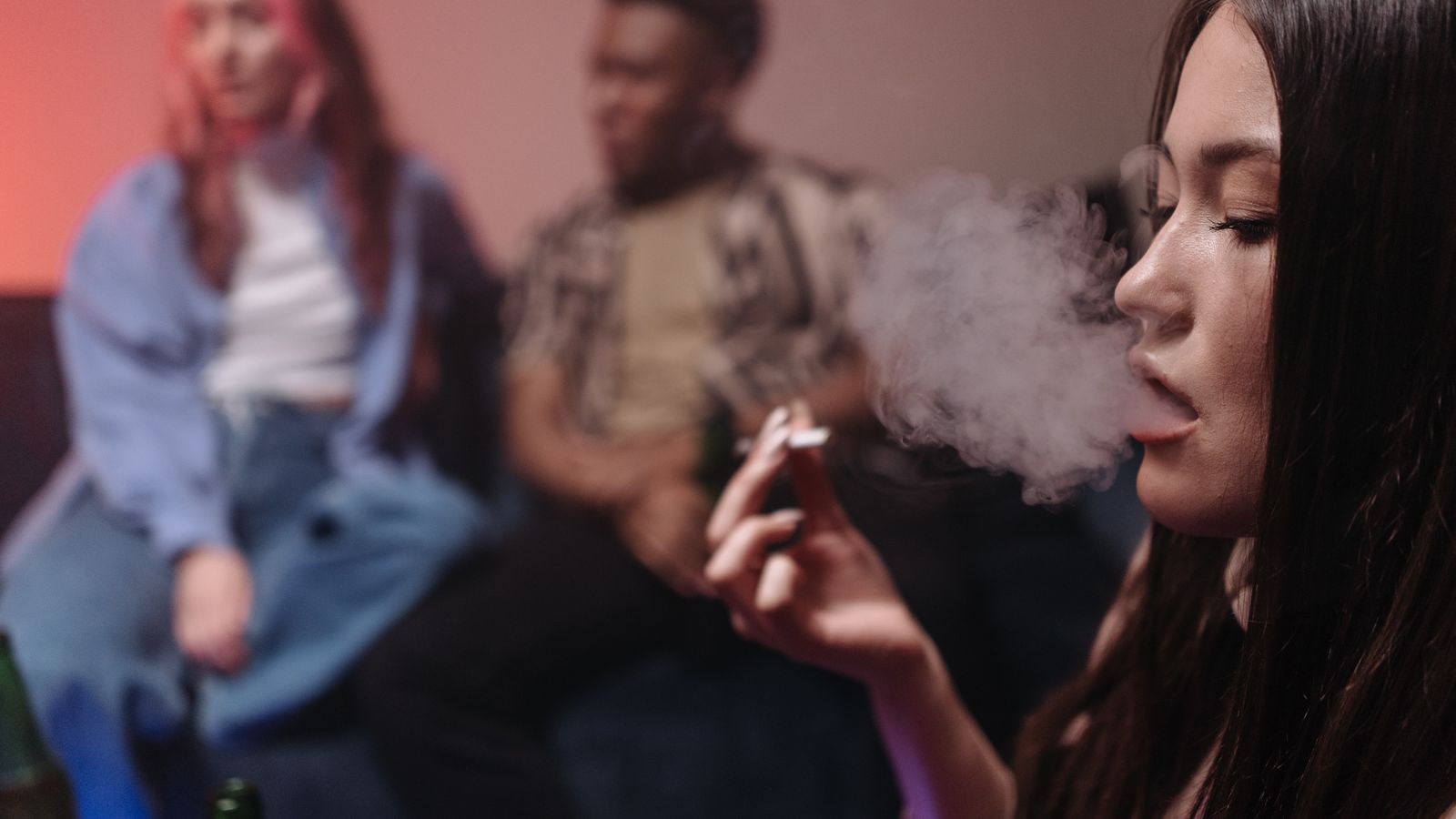 Young adults relax indoors, smoking and socializing in a casual setting.