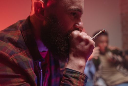 Close-up of a bearded man smoking a cannabis joint indoors with a warm ambiance.