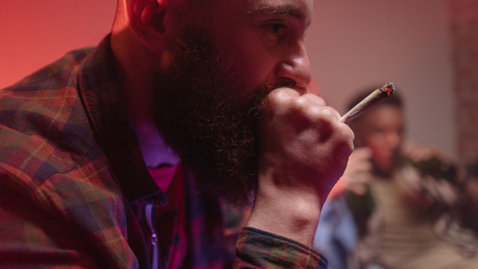 Close-up of a bearded man smoking a cannabis joint indoors with a warm ambiance.