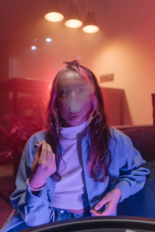 Free Woman smoking in a colorful, dimly lit indoor setting, exhaling smoke. Stock Photo