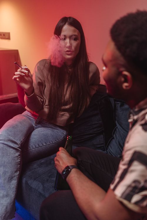 Free Young adults enjoying a casual conversation while smoking indoors on a sofa. Stock Photo