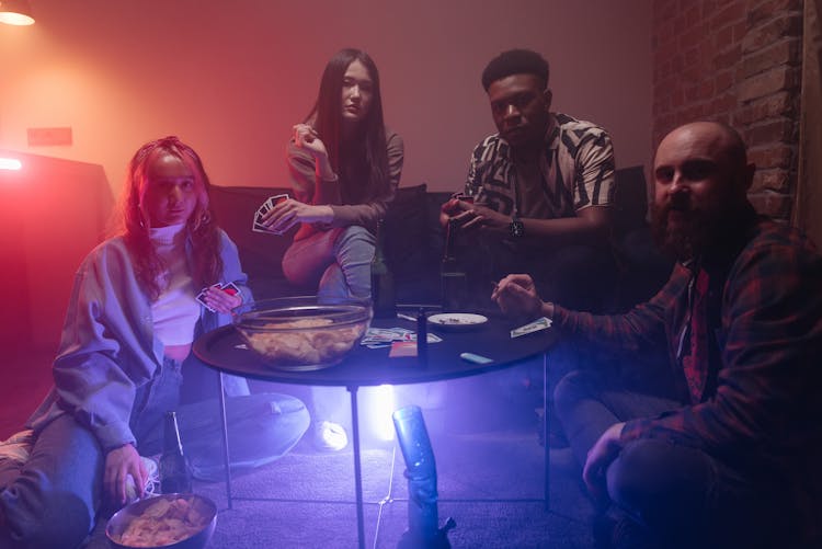 A Group Of People Playing Cards In A Dark Room