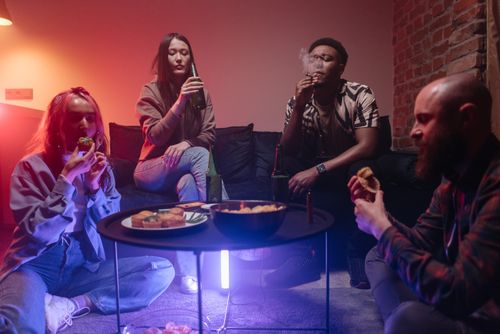Free Young adults enjoying a casual indoor gathering with snacks and drinks, featuring a relaxed and diverse atmosphere. Stock Photo