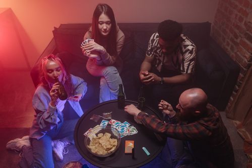 Free A lively indoor scene of friends playing cards and enjoying drinks around a table. Stock Photo