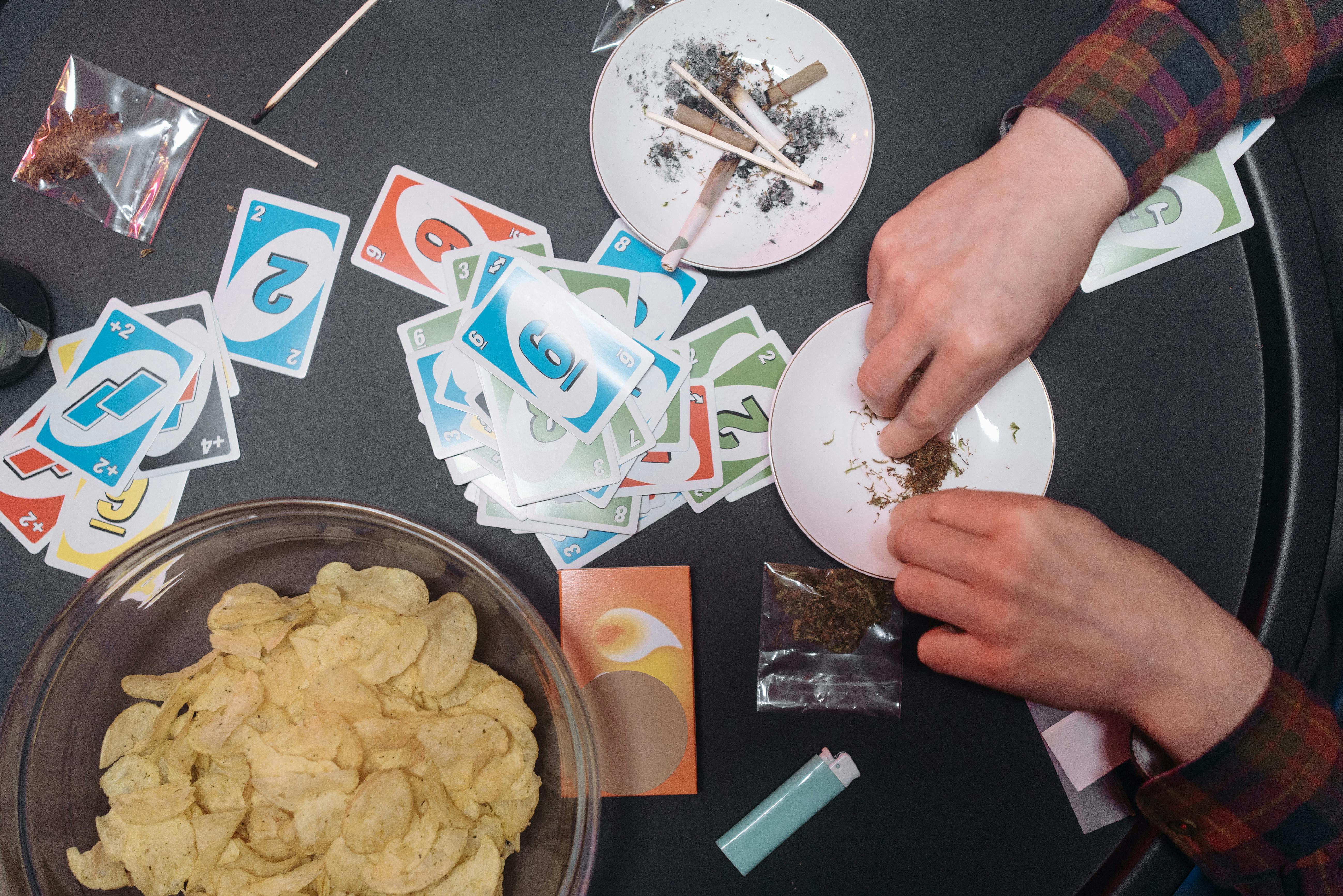 Overhead view of a table with Uno cards, potato chips, and cannabis paraphernalia.