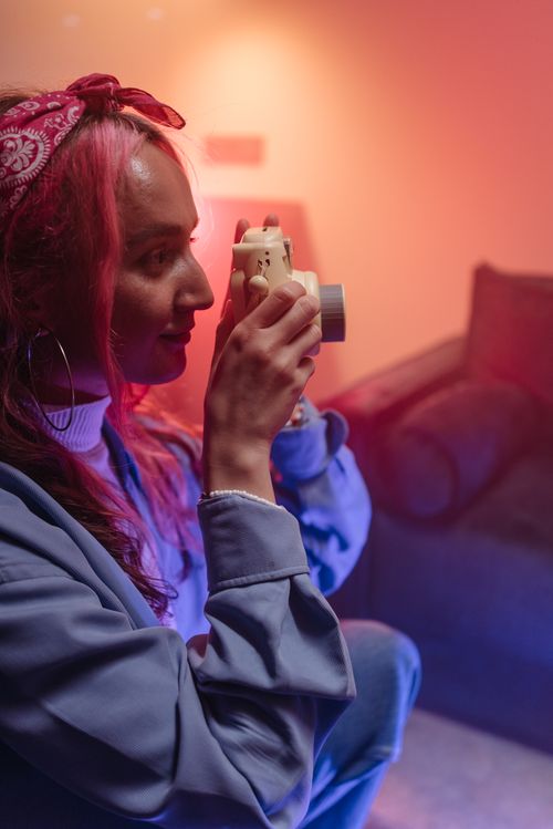 Free Young woman with colorful hair using an instant camera indoors. Stock Photo