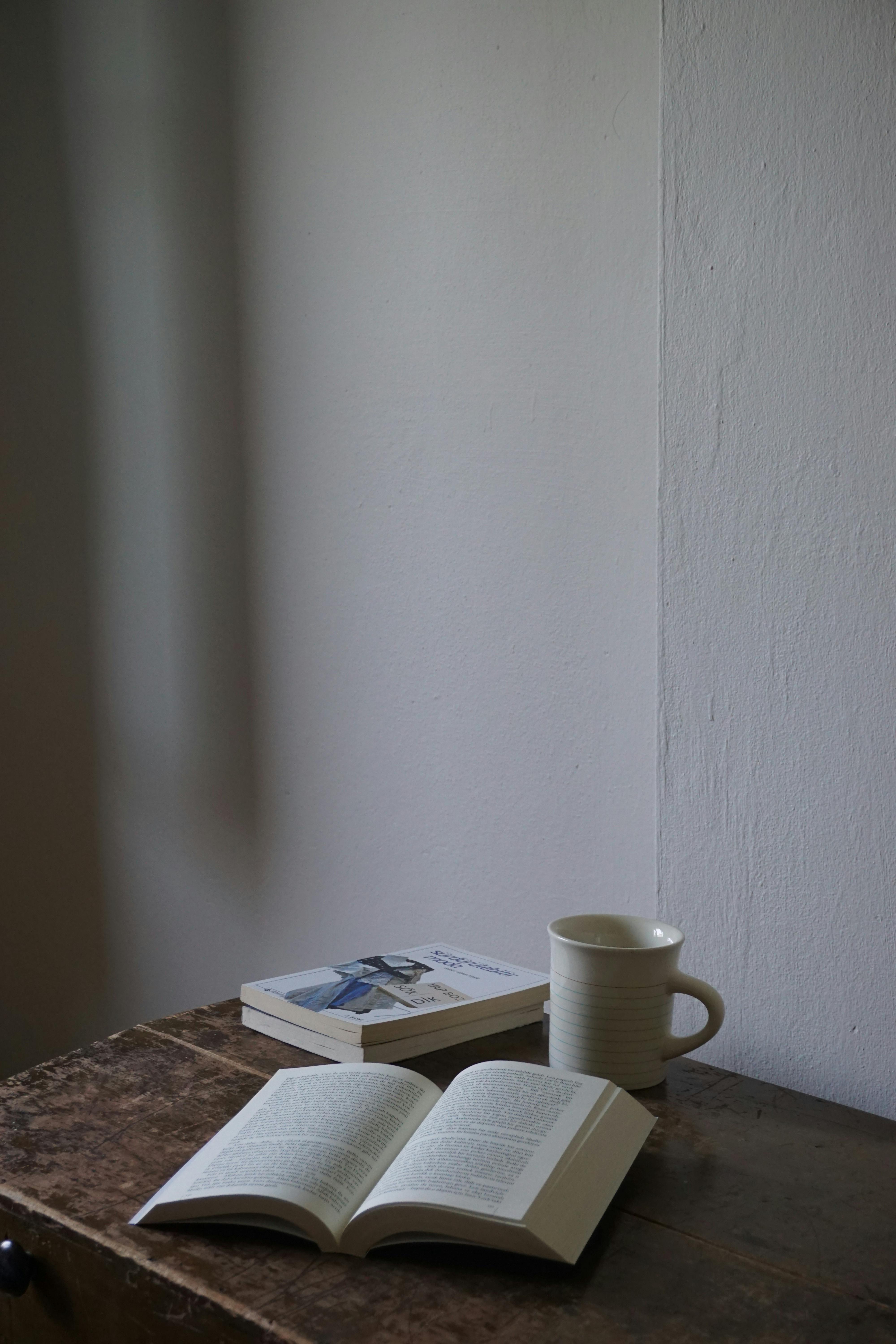 A peaceful corner with open book, closed book, and ceramic mug on wooden table.