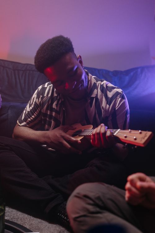 Free African American man enjoying music and playing ukulele indoors with soft lighting. Stock Photo