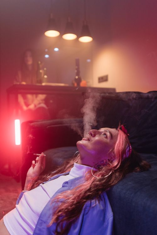 Free Woman with curly hair enjoying smoke in a cozy, moody indoor setting with atmospheric lighting. Stock Photo