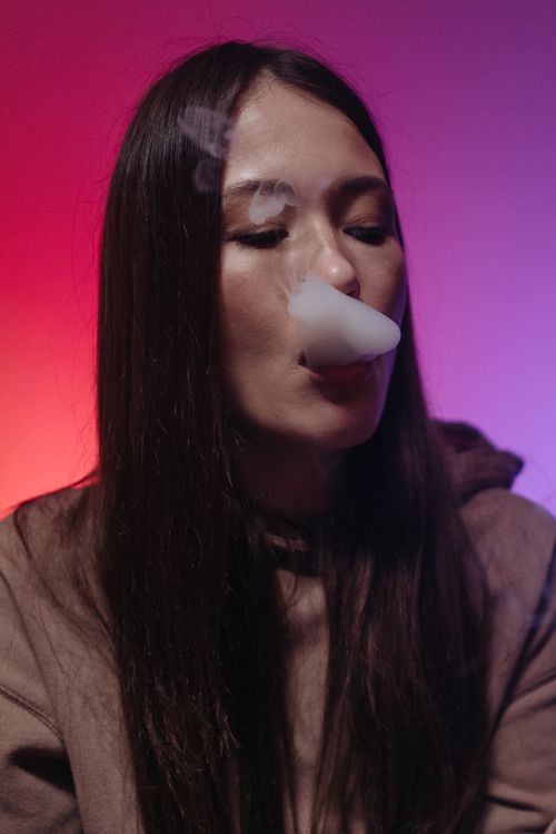 Free A woman with long hair exhales smoke, set against a colorful gradient background. Stock Photo