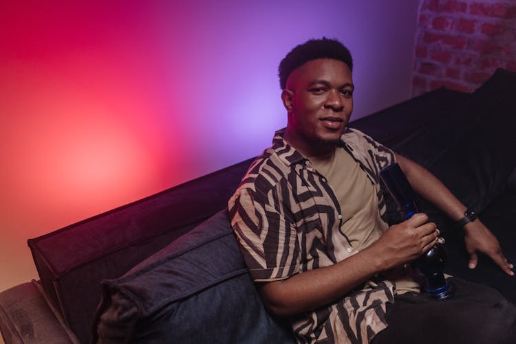 A Man Sitting On The Couch Holding A Bong