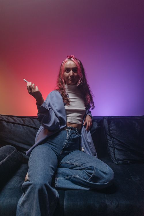 Free Young woman with pink hair relaxing on a sofa, colorful lighting creates a cozy and vibrant atmosphere. Stock Photo