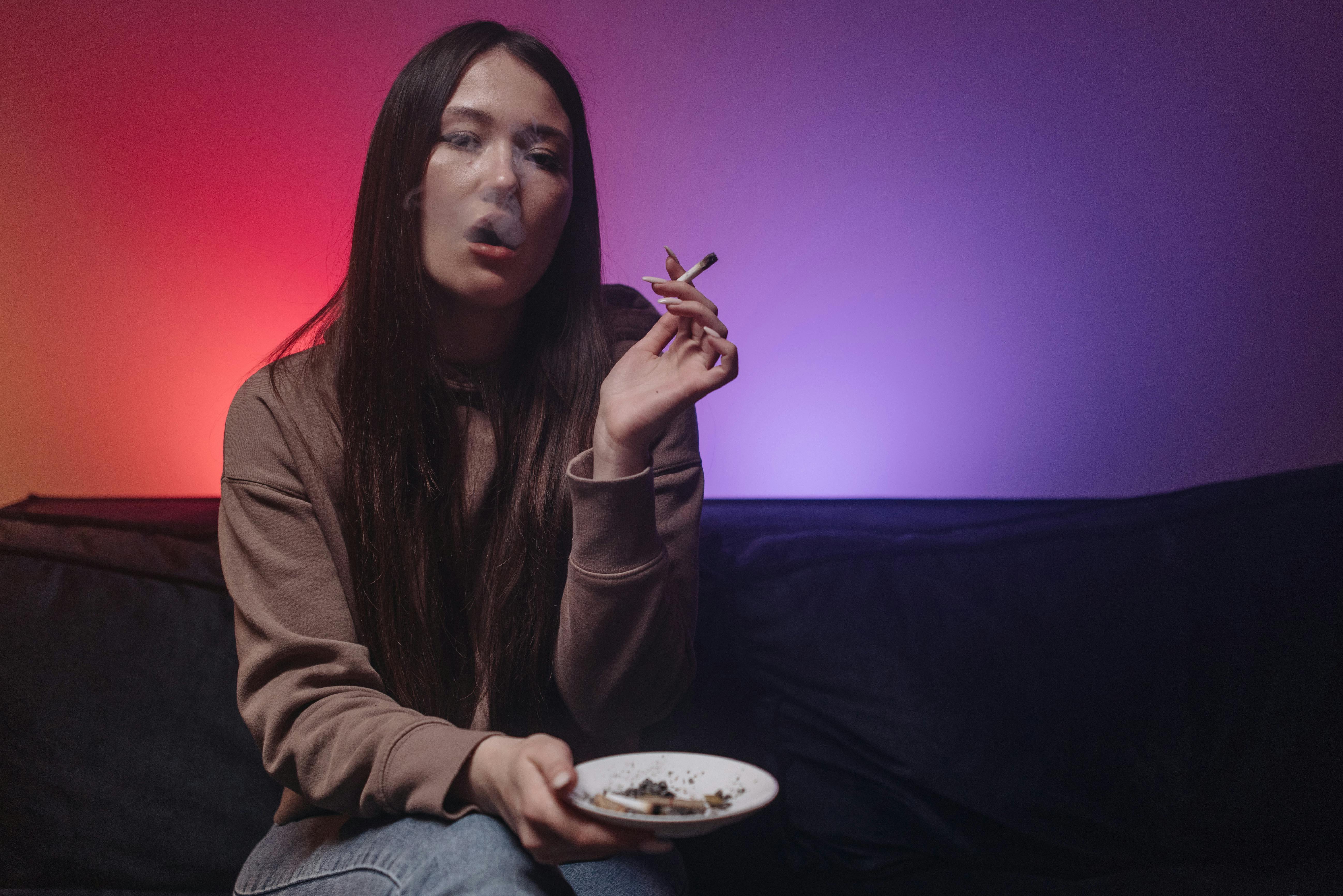 A woman smoking in a neon-lit room, seated on a couch, exuding calm vibes.