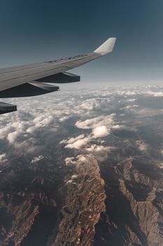 View from an airplane wing of clouds and rugged terrain below, capturing a scenic flight.
