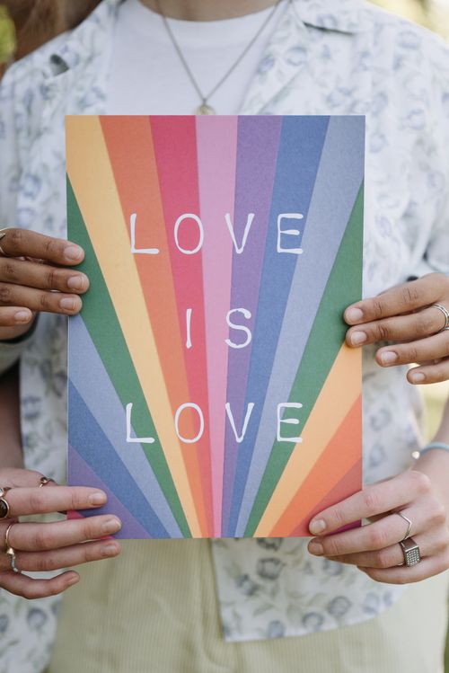 Free A vibrant rainbow-colored poster with the text 'Love is Love' held by diverse hands, symbolizing unity. Stock Photo