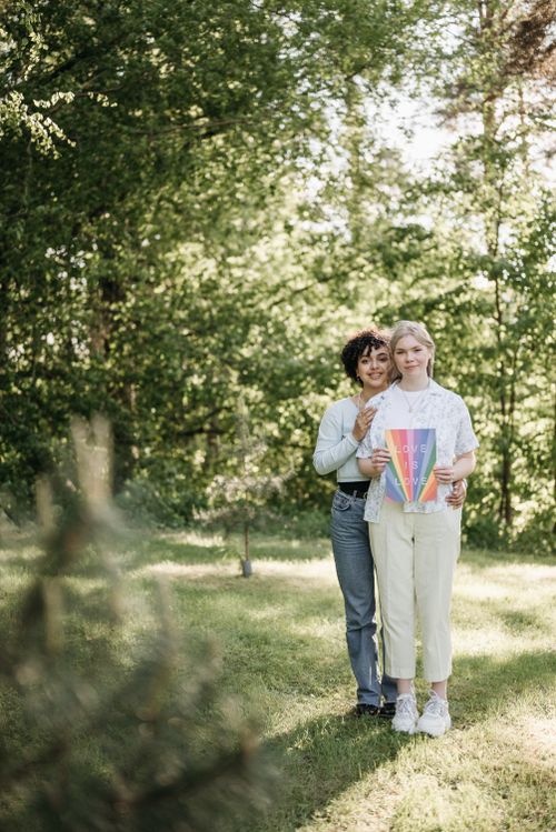 Free Two women embrace holding a colorful LGBT pride poster in a sunny park. Stock Photo